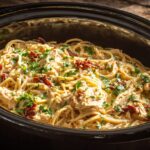 Top-down view of creamy, cheesy spaghetti crock pot chicken garnished with fresh parsley.