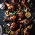Overhead view of crispy baked chicken drumsticks recipe on dark slate with herbs and lemon