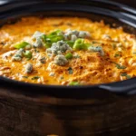 A top-down view of creamy buffalo chicken dip in crock pot surrounded by tortilla chips and celery.